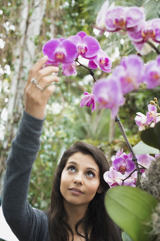 a young woman reaching up to touch an orchid in a L5V5X2F min